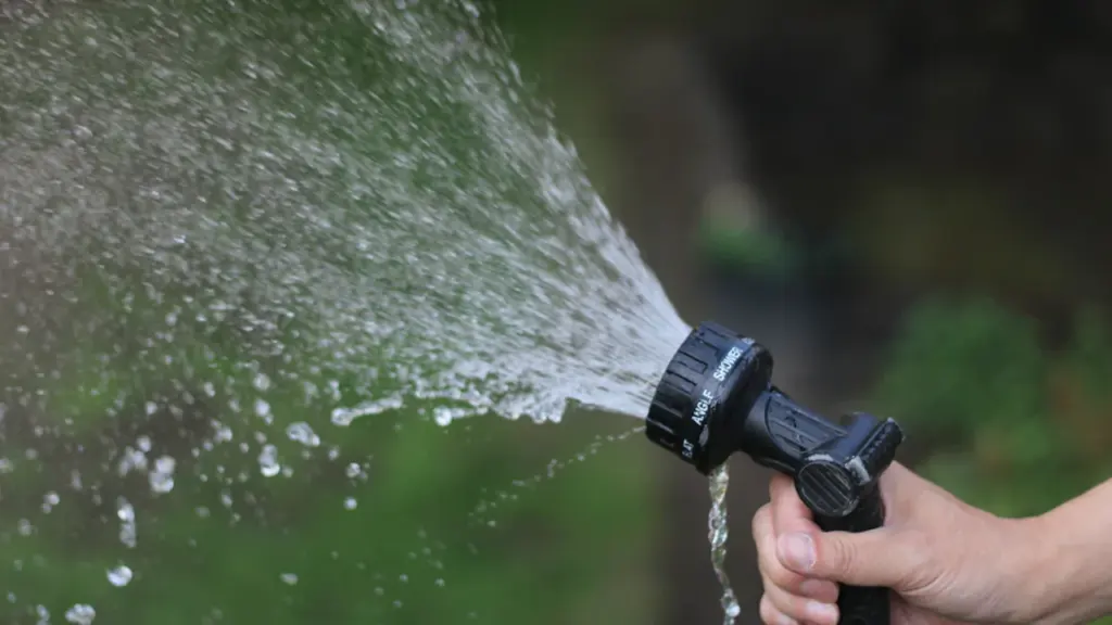 Main d'une personne utilisant un pistolet d'arrosage pour arroser son jardin.