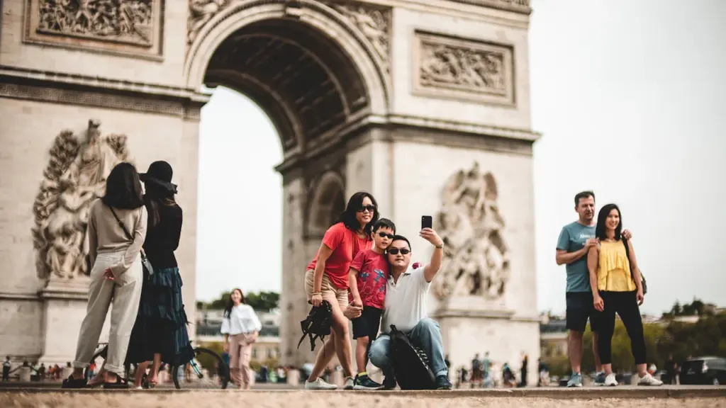 Une famille prend un selfie devant l'Arc de Triomphe à Paris sous le soleil.
