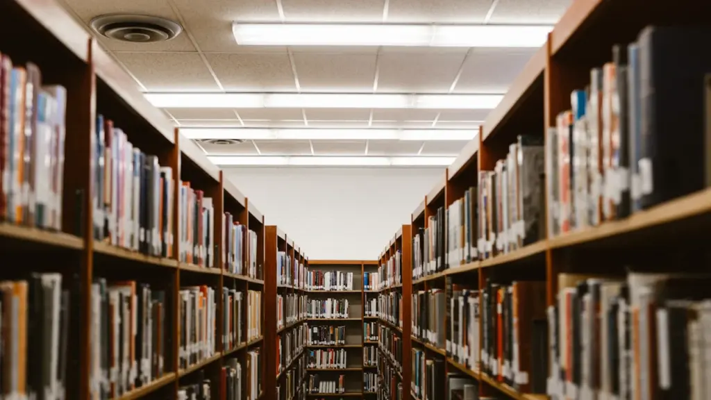 Allées de bibliothèque avec rayonnages remplis de livres sous un éclairage néon.