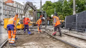 Des ouvriers en gilets orange travaillent sur des rails de tramway avec des pelles.