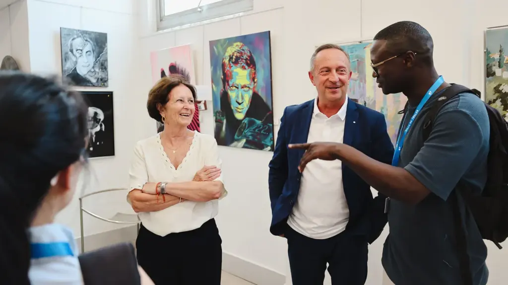 Trois personnes discutent joyeusement dans une galerie d'art entourées de tableaux colorés aux murs.