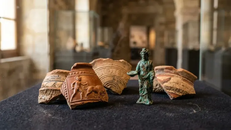 Une statuette en bronze entourée de fragments de poterie antique exposée dans un musée.
