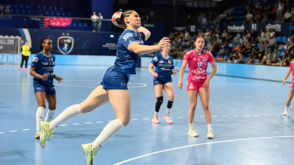 Une joueuse de handball en plein saut tire le ballon en plein match indoor.