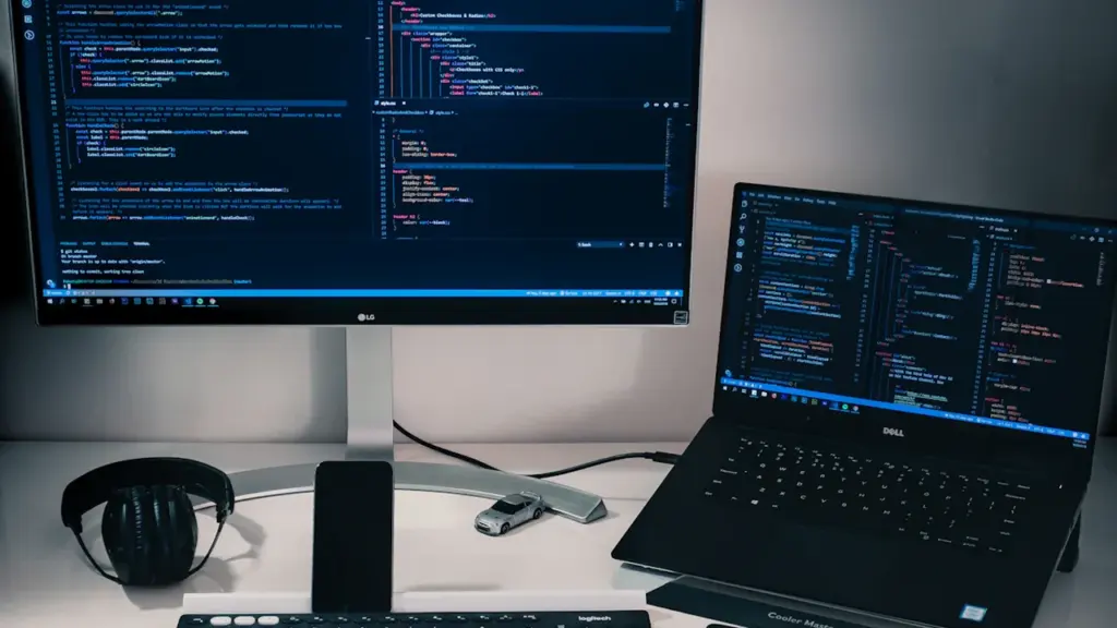 Un bureau informatique moderne avec écran et ordinateur portable affichant du code informatique.