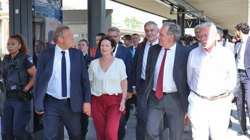 Un groupe de personnalités politiques marchant sur un quai de gare avec un agent.