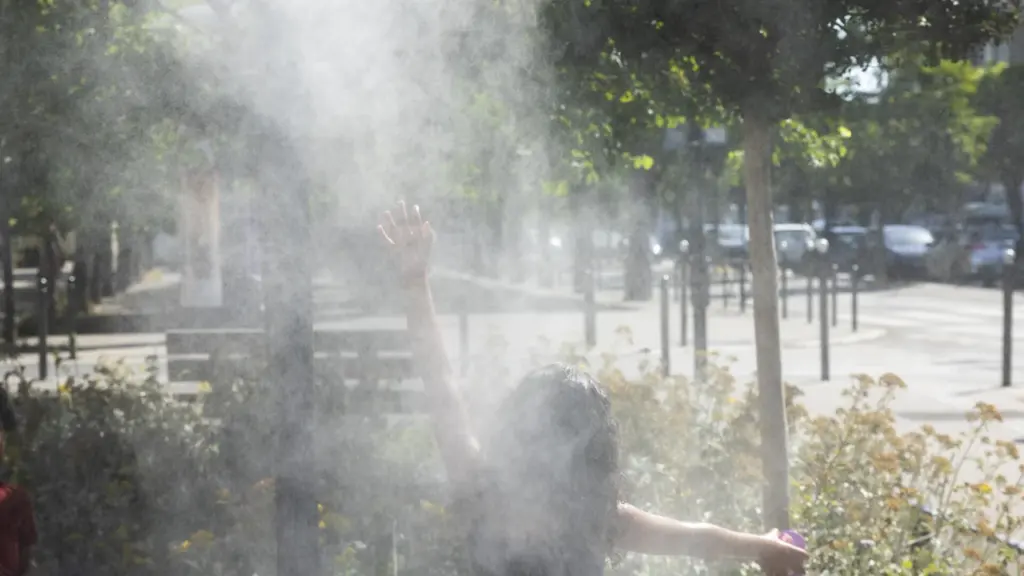 Une jeune fille joue en levant les bras dans une fine brume rafraîchissante extérieure.