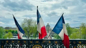Trois drapeaux français flottant devant un monument historique emblématique à Paris.