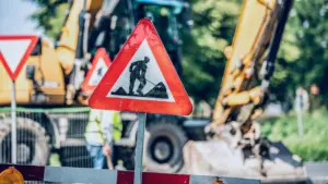 Panneau de signalisation travaux avec une pelleteuse jaune en arrière-plan flou.