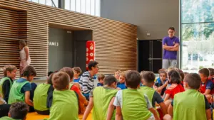 Un groupe d'enfants assis dans un gymnase écoutant attentivement une femme âgée.