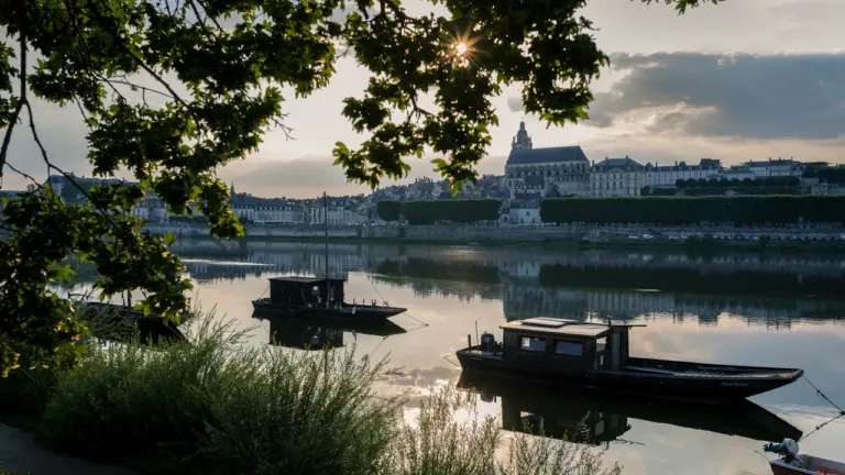 Deux bateaux traditionnels sur la Loire devant la ville de Blois au coucher du soleil.