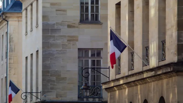 Bâtiment administratif avec deux drapeaux français flottant devant une façade en pierre.