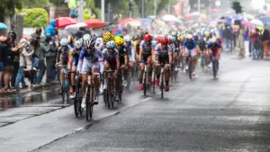 Un peloton de cyclistes professionnels roule sous la pluie lors d'une course sur route.