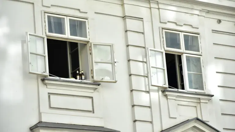 Fenêtres ouvertes sur une façade de bâtiment blanc sous un soleil intense.