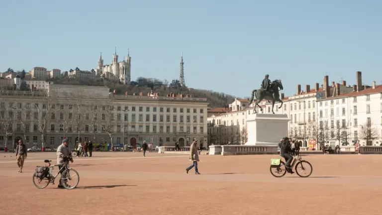 Des personnes à vélo et à pied sur une grande place à Lyon.