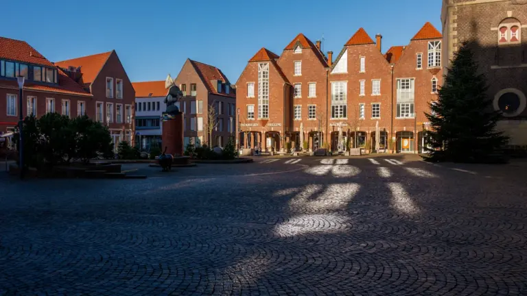 Une place pavée historique entourée de bâtiments en briques sous la lumière du soleil.
