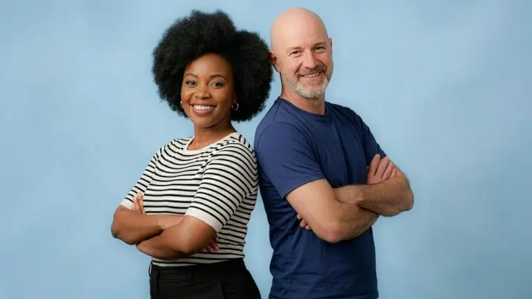 Une femme noire et un homme blanc souriants, posant dos à dos, bras croisés.