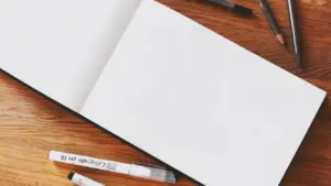 Cahier de dessin ouvert avec des crayons et stylos sur une table en bois.