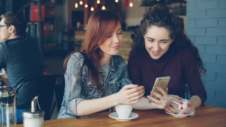 Deux amies discutent joyeusement autour d'un café dans un établissement moderne à Grenoble.