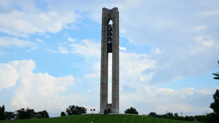 Une tour de carillon monumentale sur une colline herbeuse sous un ciel bleu.
