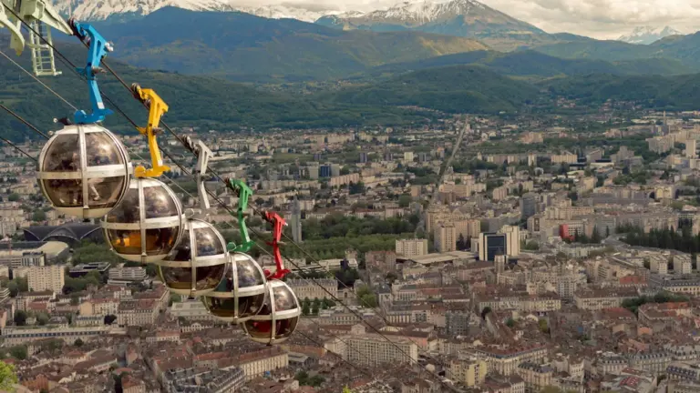 Vue panoramique du téléphérique de Grenoble survolant la ville avec les montagnes en arrière-plan.