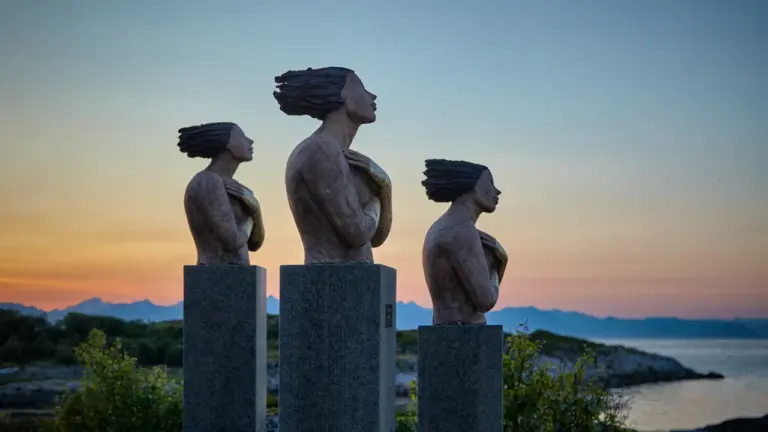 Trois sculptures contemporaines en extérieur face à un coucher de soleil sur la mer.