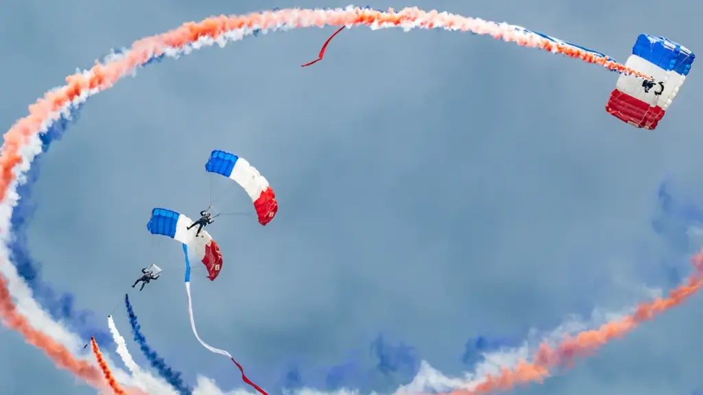 Des parachutistes militaires français réalisant des figures acrobatiques avec des fumigènes tricolores.