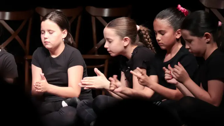 Un groupe de jeunes enfants en tenue noire répétant sur scène au théâtre.