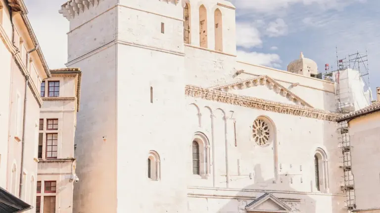 Une grande église en pierre beige domine une place animée avec des piétons et terrasses.