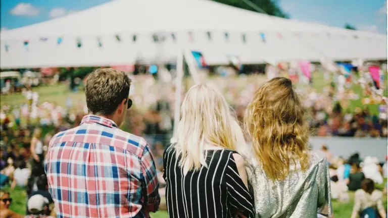 Des jeunes adultes regardent un festival en plein air sous un grand chapiteau blanc.