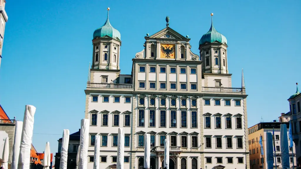 Bâtiment historique européen imposant avec une horloge sur une place publique ensoleillée.