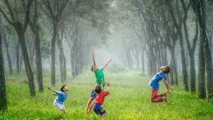Quatre jeunes enfants jouent joyeusement au ballon dans un parc boisé verdoyant.
