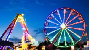 Grande roue illuminée et manèges de fête foraine dans la nuit.