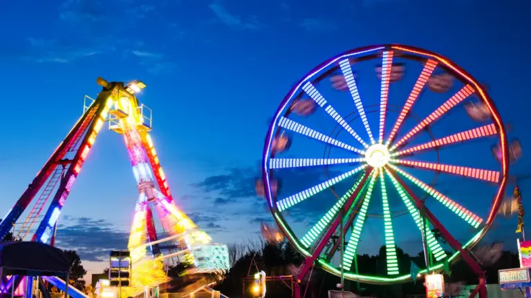 Grande roue illuminée et manèges de fête foraine dans la nuit.