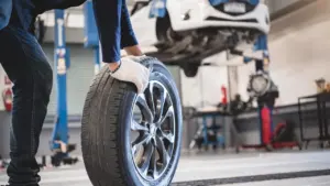Un mécanicien portant des gants de protection manipule une roue de voiture dans l'atelier.