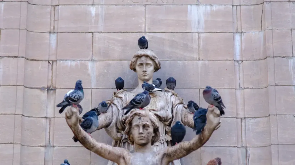 Plusieurs pigeons perchés sur une statue en pierre ancienne dans un cadre urbain.